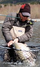 Fly fisherman with a steelhead in a net and pole in his mouth/